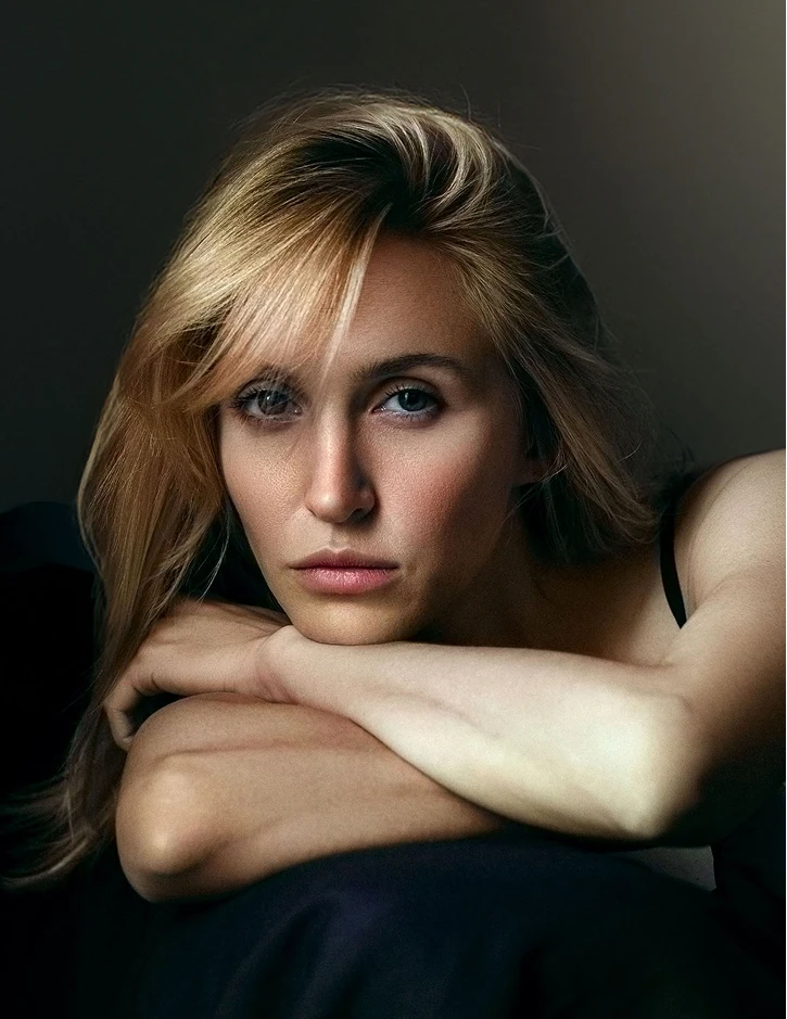 Blonde woman with blue eyes resting arms on dark surface in contemplative portrait photography