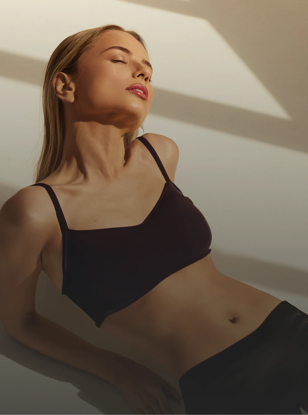 Woman in black sports bra relaxing in sunlight with eyes closed and peaceful expression