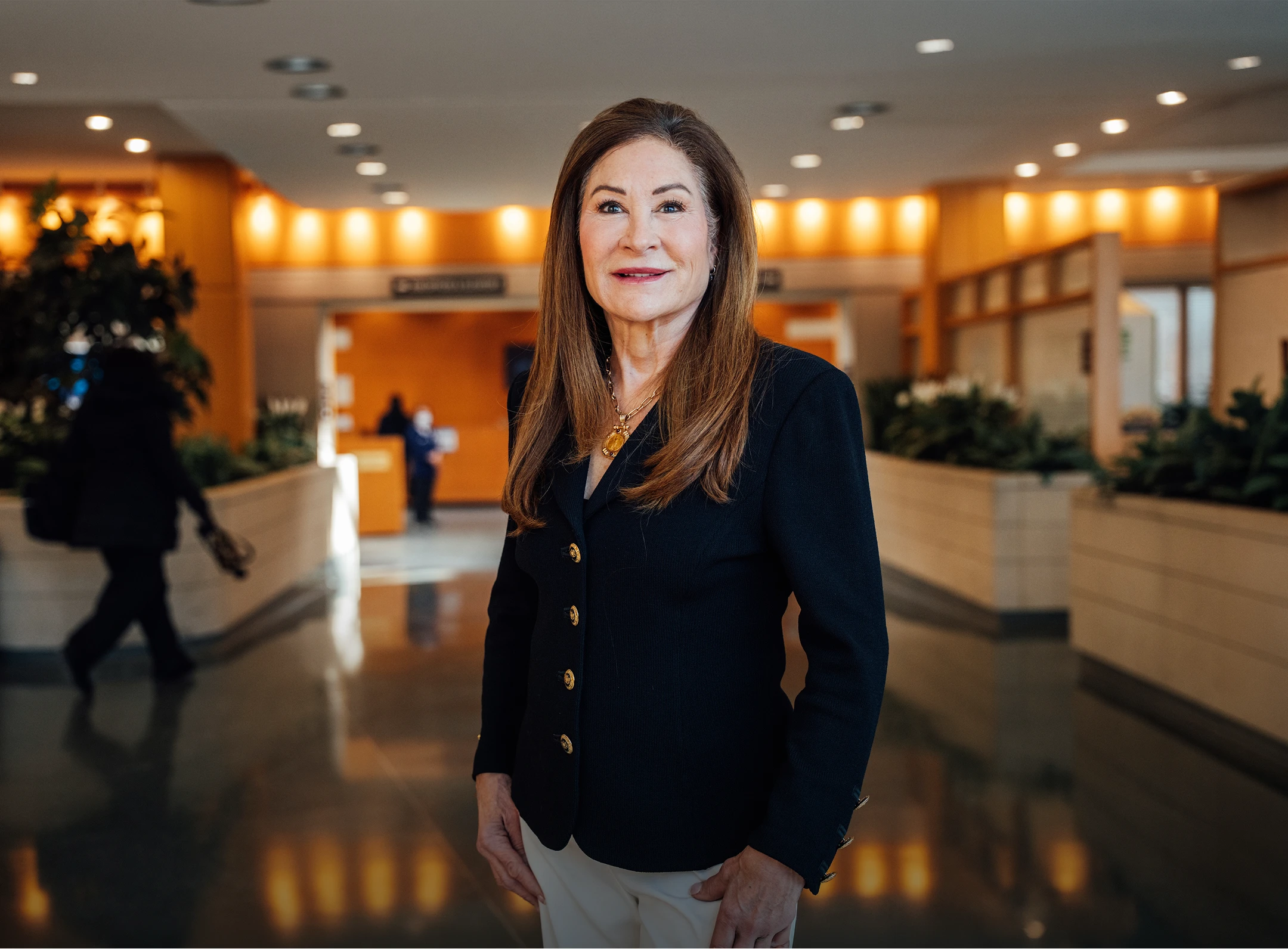 Professional woman in business attire standing in modern office lobby with warm lighting and blurred background