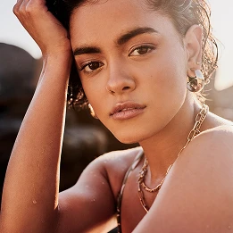 Woman wearing gold chain necklace and hoop earrings with natural makeup in warm sunlight