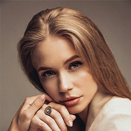 Young woman with long blonde hair wearing statement ring, professional beauty portrait on neutral background