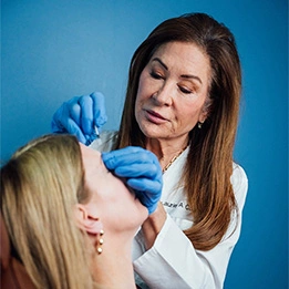 Laurie A. Casas, MD in blue gloves administering cosmetic injection to female patient in clinical setting