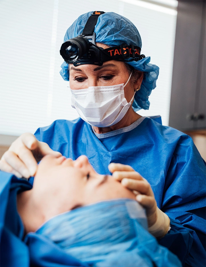 Surgeon performing cosmetic procedure on patient in operating room wearing surgical mask and protective gear