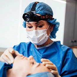 Laurie A. Casas, MD performing dental procedure wearing surgical mask, scrubs and headlamp in medical office