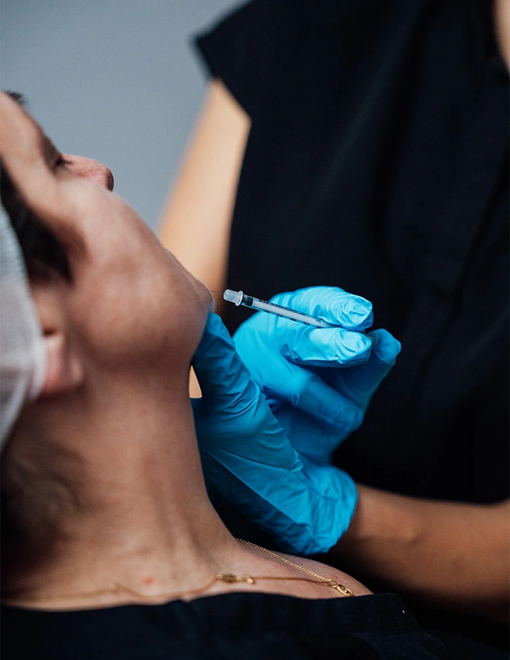 Healthcare professional administering neck injection to patient wearing blue medical gloves
