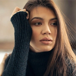 Woman in black turtleneck sweater with long dark hair posing with hand near face in soft natural lighting