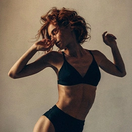 Woman dancing in black sports bra and underwear with flowing hair against neutral background