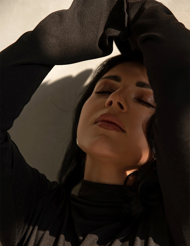 Woman in black hoodie looking up with hands adjusting hood, dramatic low angle perspective