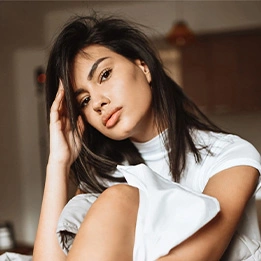 Beautiful woman with dark hair in white t-shirt posing indoors with hand near face in natural lighting