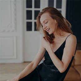 Woman in black dress showing toned arms while smiling and posing elegantly indoors