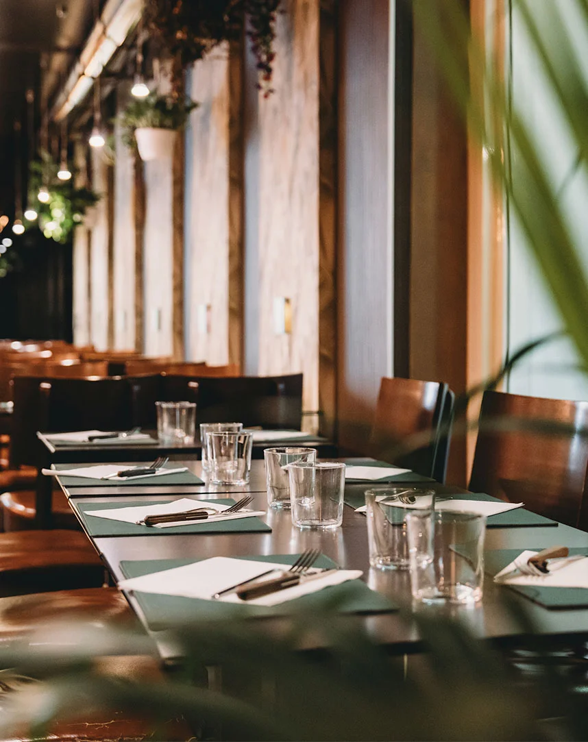 Elegant restaurant interior with long dining table set with glasses and place settings, warm lighting and modern decor